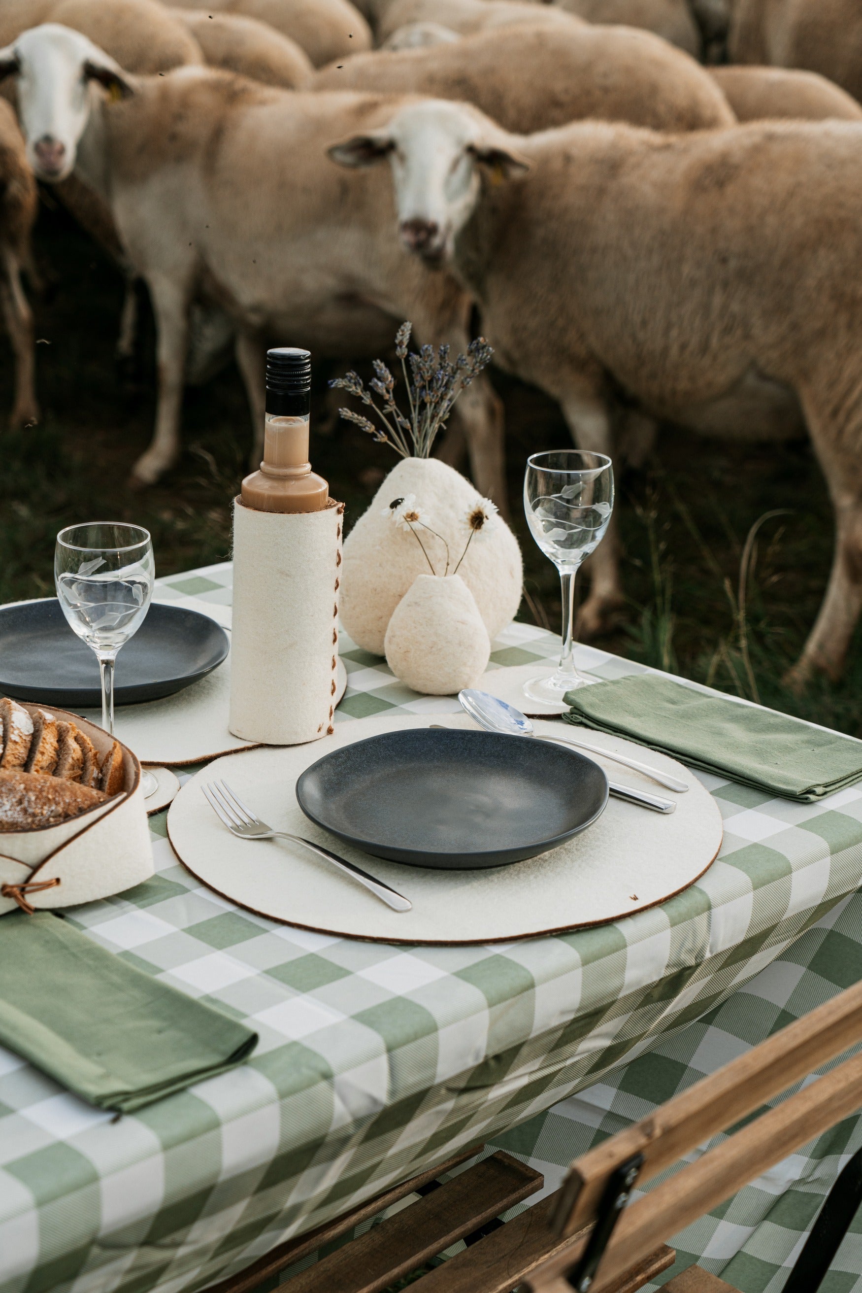 Minimalist outdoor table setting with natural wool bottle sleeve and sheep pasture